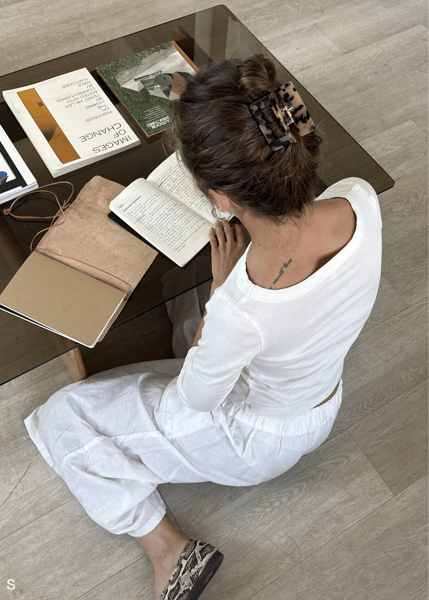 Woman sitting at a coffee table with books and a notebook, wearing a tortoiseshell hair clip.
