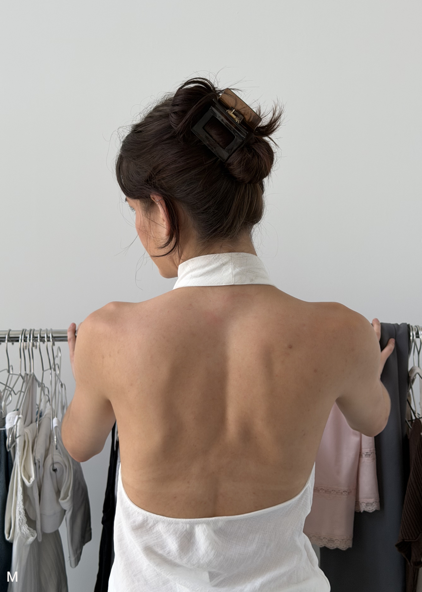 Person wearing a brown hair clip in front of a rack of clothes against a plain background.