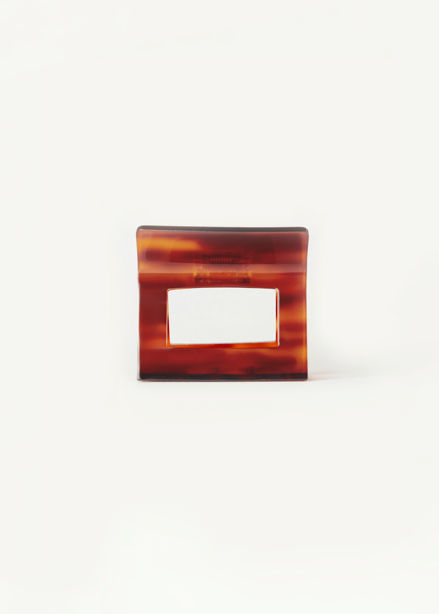 A square red-toned tortoiseshell claw clip with a rectangular cutout in the centre shown on a plain white background.
