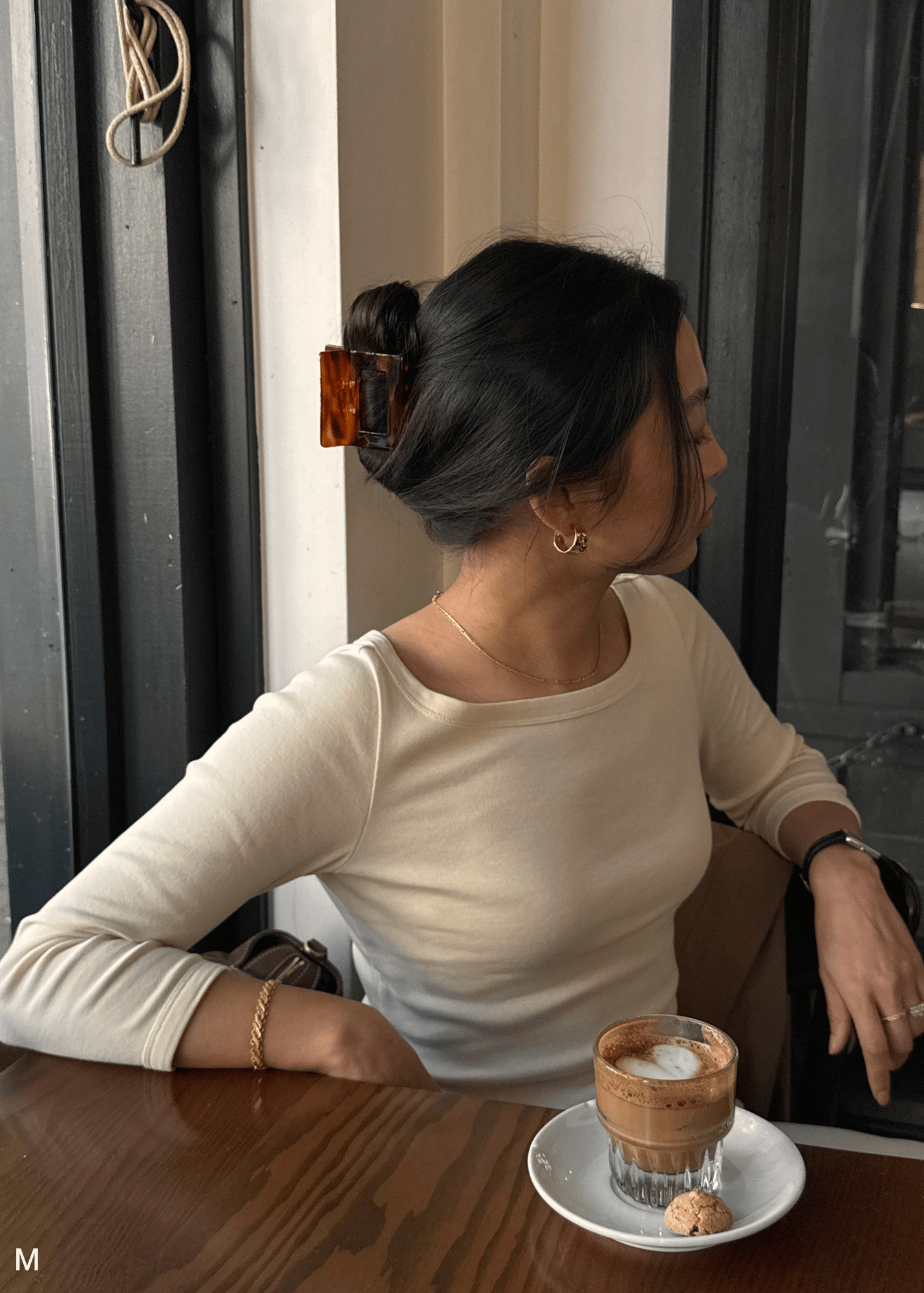 Woman wearing a hair clip sitting at a table with a cup of coffee in a cafe.
