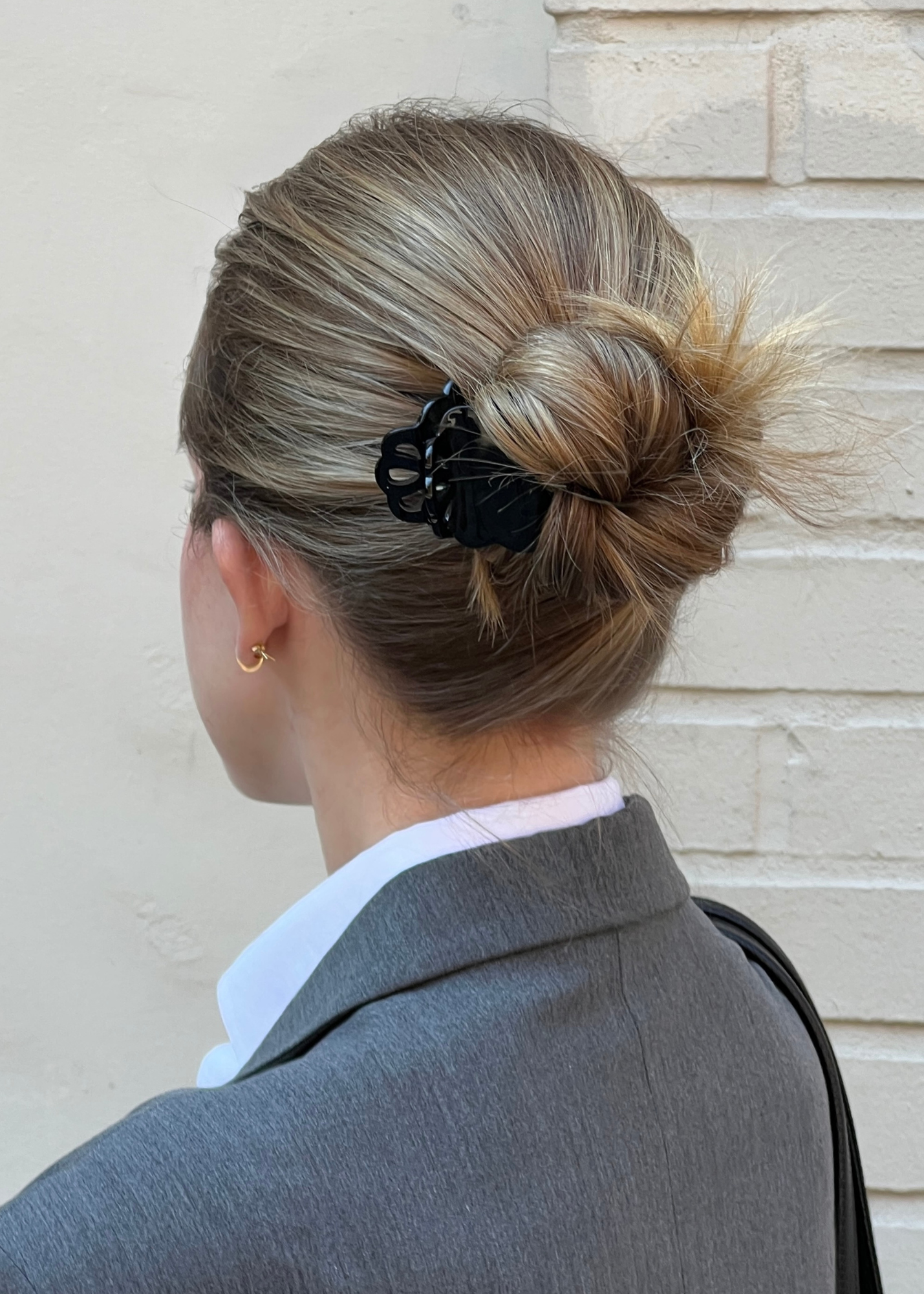 Person with a stylish hair bun wearing a black scalloped claw clip, standing against a light-coloured wall.