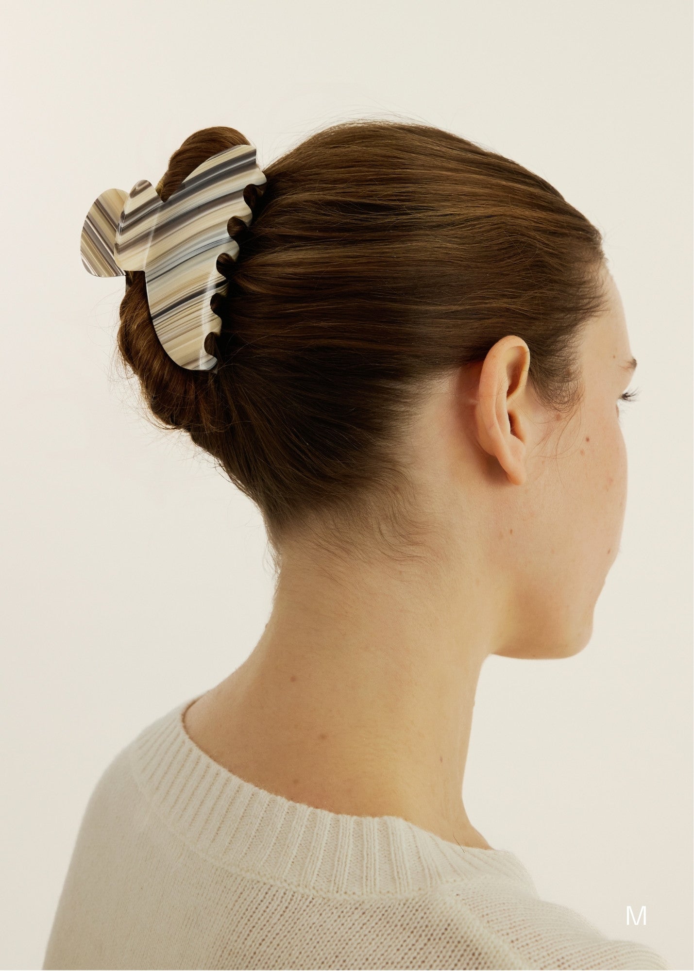 Woman with a medium-sized striped claw clip securing her up-do against a plain background