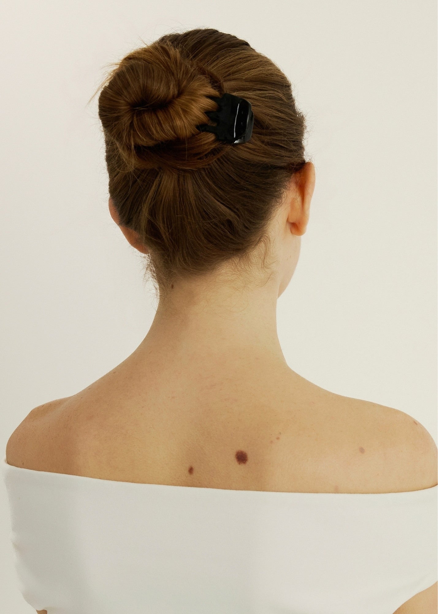 Back view of a person with a neatly styled bun secured with a small black hair clip on a plain background