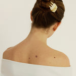 Woman with a bun secured with a beige-coloured hair clip on a plain background
