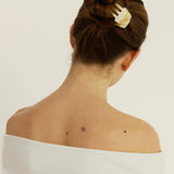 Woman with a bun secured with a beige-coloured hair clip on a plain background