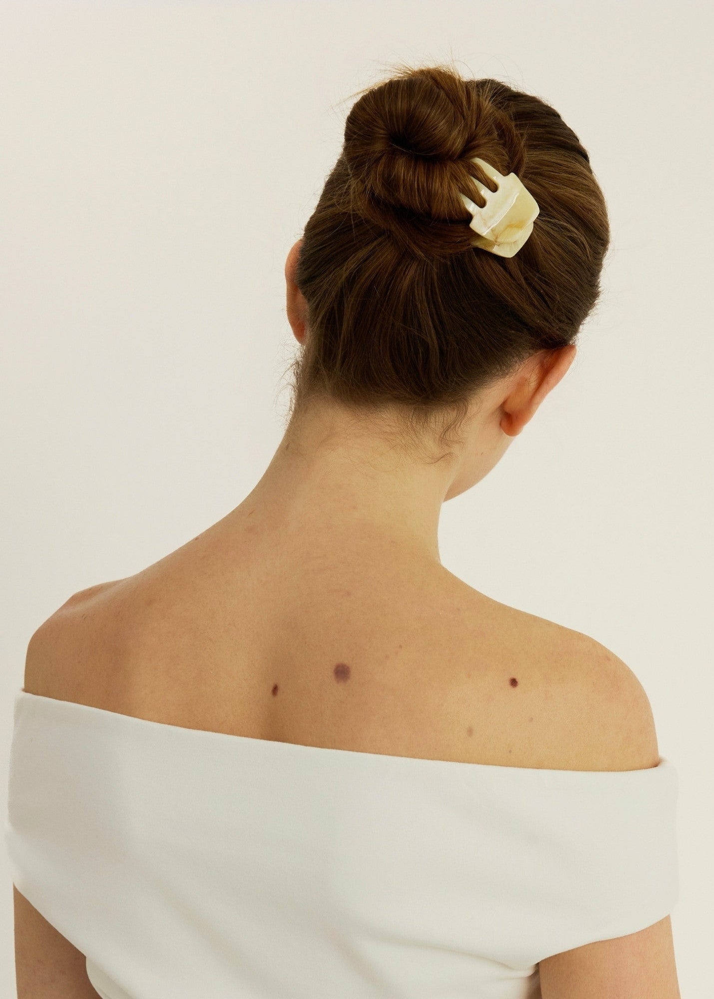 Woman with a bun secured with a beige-coloured hair clip on a plain background
