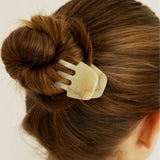 Close-up of a small beige hair clip holding up a bun with a neutral background