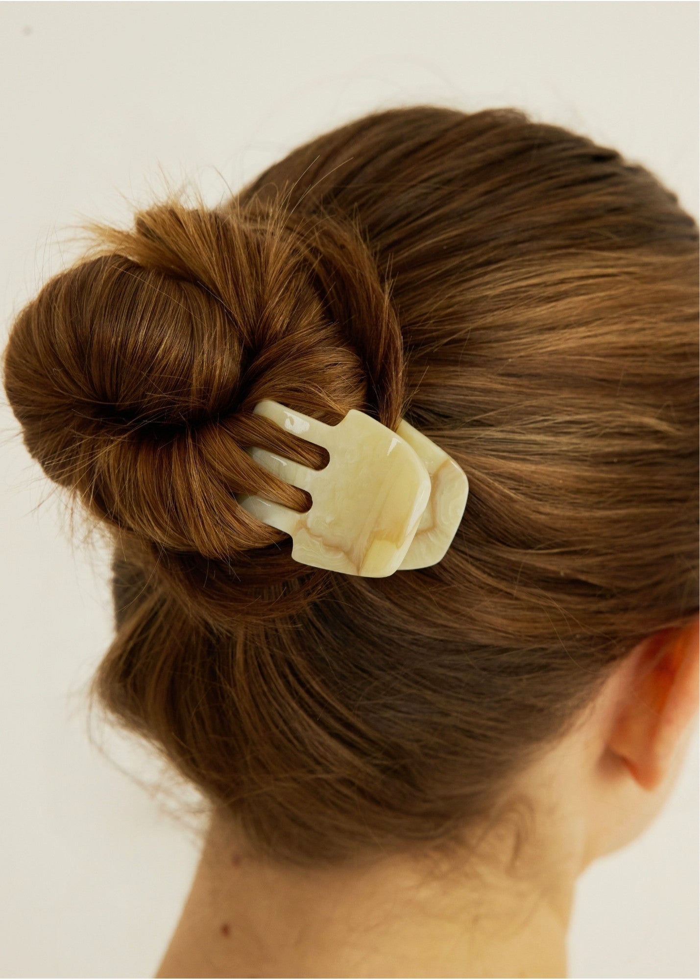 Close-up of a small beige hair clip holding up a bun with a neutral background
