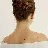 Back view of a person with a neatly styled bun secured with a small tortoise-coloured hair clip wearing a white off-shoulder top on a light background