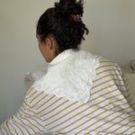 Woman with dark curly hair secured with a small tortoise-coloured hair clip wearing a white with yellow stripes shirt and a lace collar