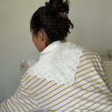 Woman with dark curly hair secured with a small tortoise-coloured hair clip wearing a white with yellow stripes shirt and a lace collar