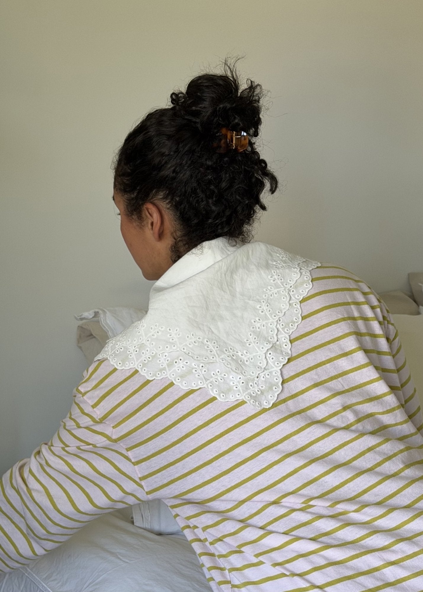 Woman with dark curly hair secured with a small tortoise-coloured hair clip wearing a white with yellow stripes shirt and a lace collar