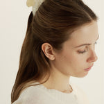 Woman with a half-up, half-down hairstyle wearing a shell inspired claw clip and a white sweater against a beige background