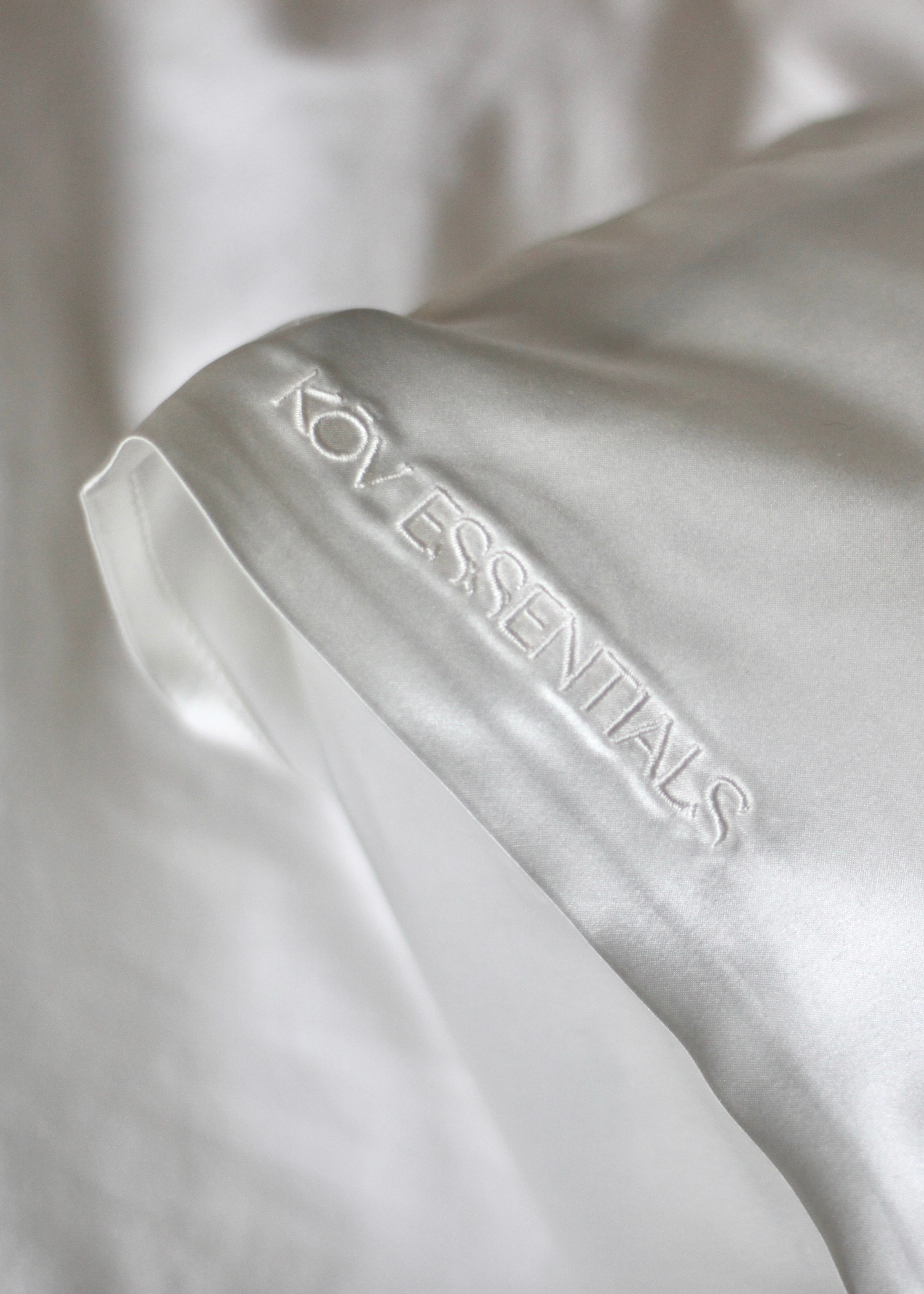 A white silk pillow case with Kov Essentials embroidered