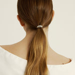 Woman with long brown hair tied into a ponytail styled with a silver croissant-shaped hair accessory against a white background