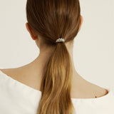 Woman with long brown hair tied into a ponytail styled with a silver croissant-shaped hair accessory against a white background