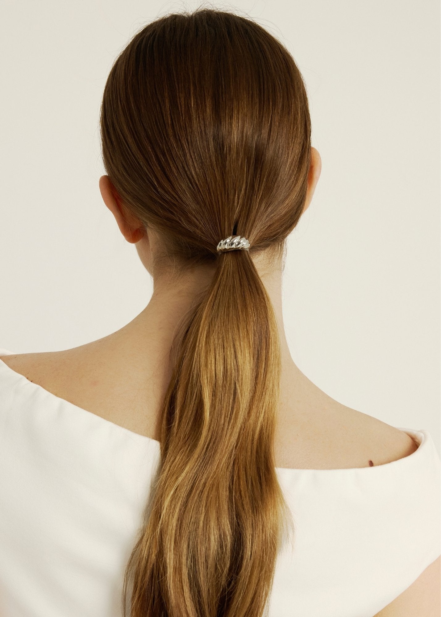 Woman with long brown hair tied into a ponytail styled with a silver croissant-shaped hair accessory against a white background
