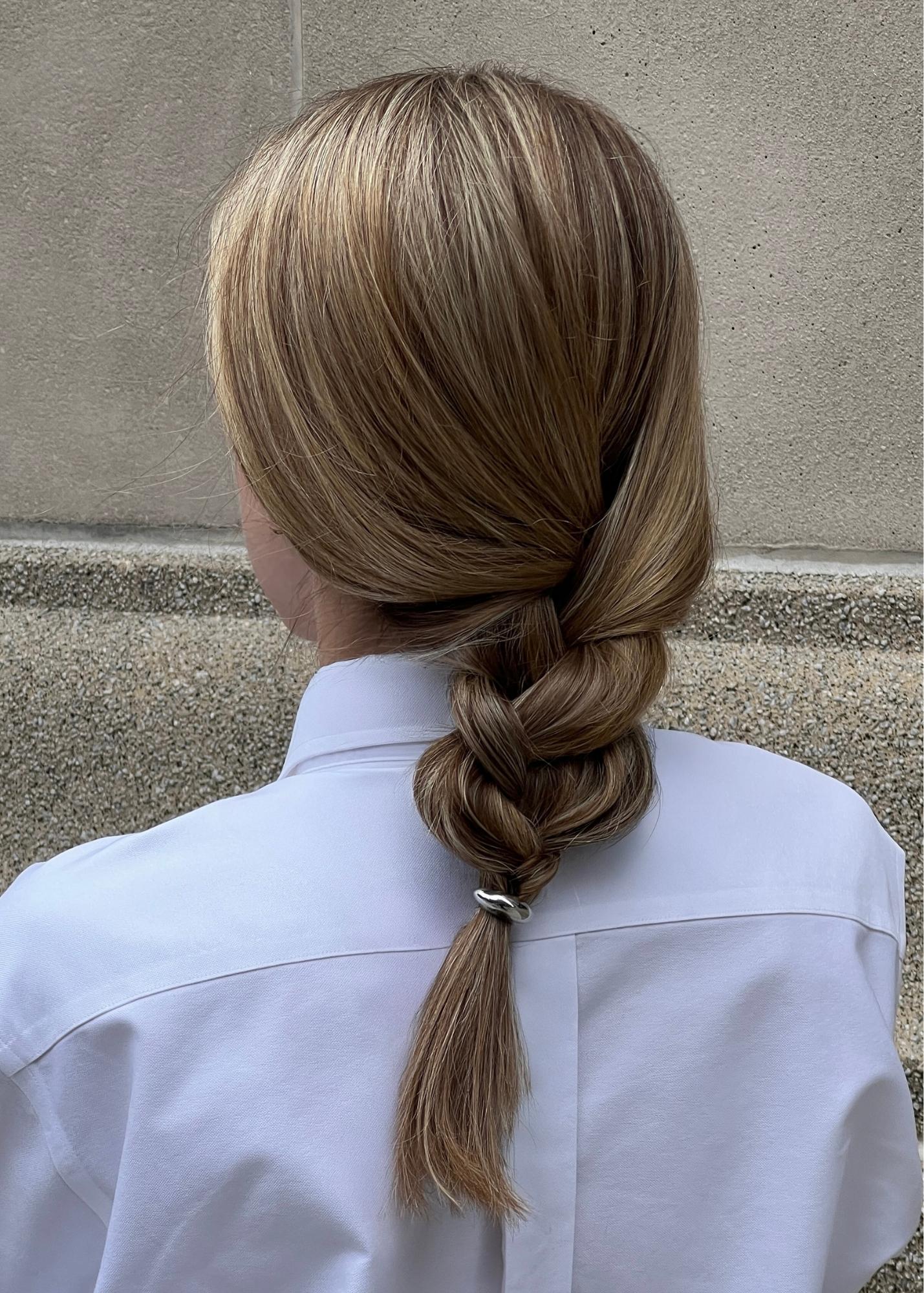 Woman with a braided hairstyle styled with a silver hair accessory wearing a white shirt against a beige wall.