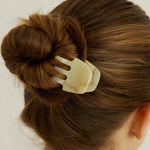 Woman with dark brown hair styled in a bun secured with the Sculpt Clip in Oak, wearing a white tank top against a white background