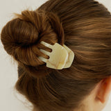 Woman with dark brown hair styled in a bun secured with the Sculpt Clip in Oak, wearing a white tank top against a white background