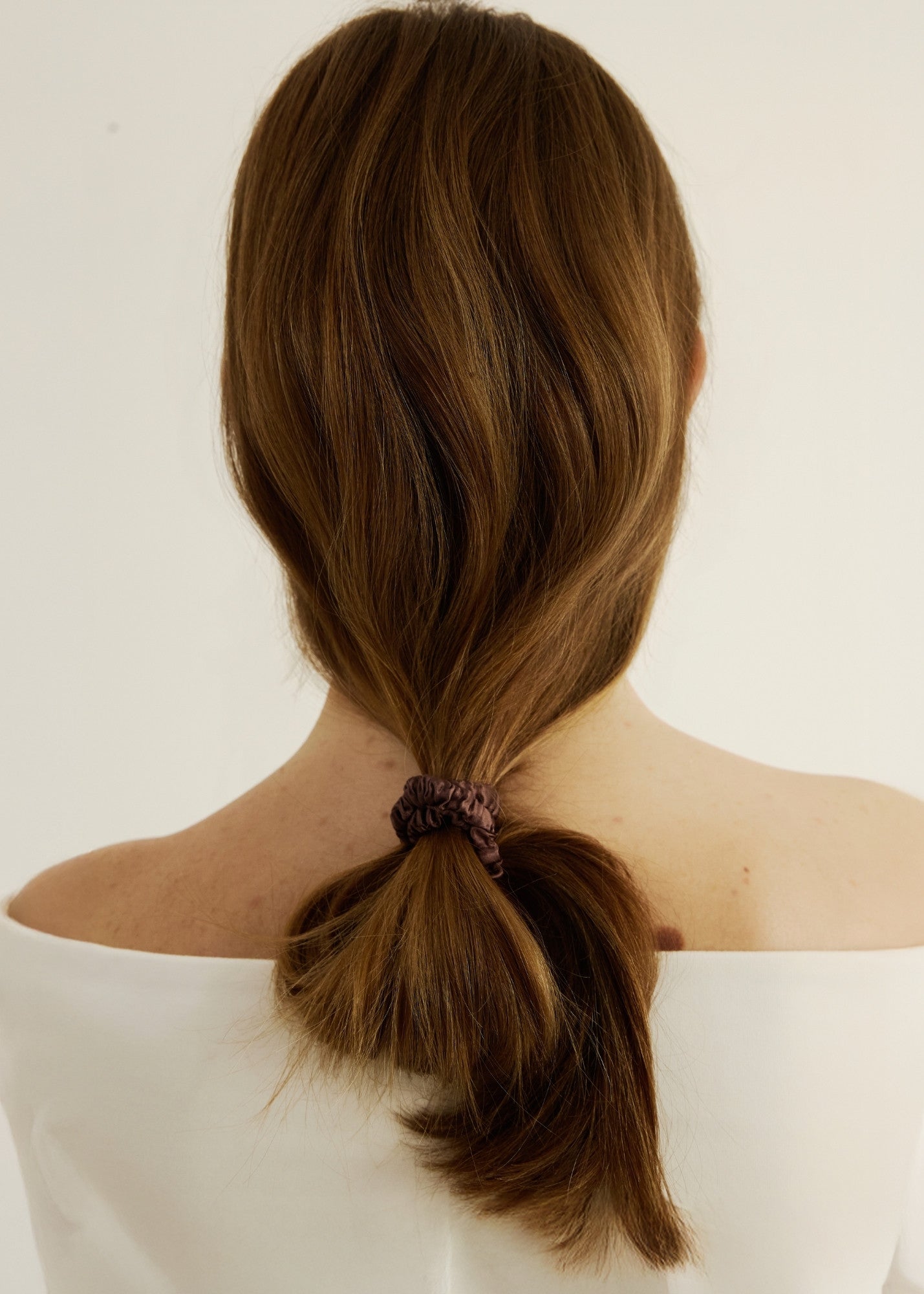 Woman with brown hair styled in a unique ponytail secured with the silk hair tie in espresso