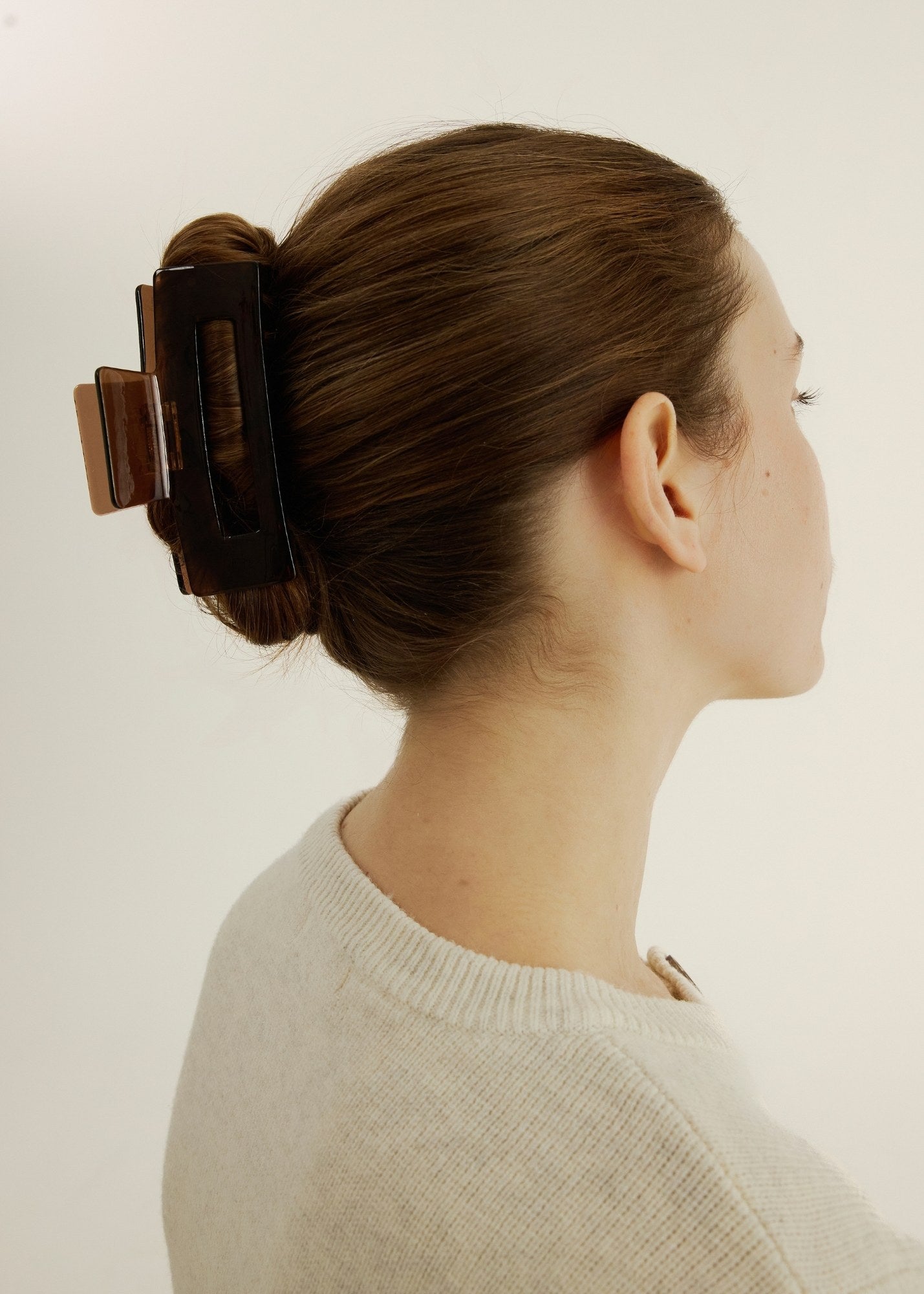 Woman with a hair clip in her bun against a plain background