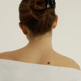 Woman with long hair tied styled half-up, half-down secured with a small black hair clip that has scalloped edges and tear drop shaped cut outs, wearing a white tank top.