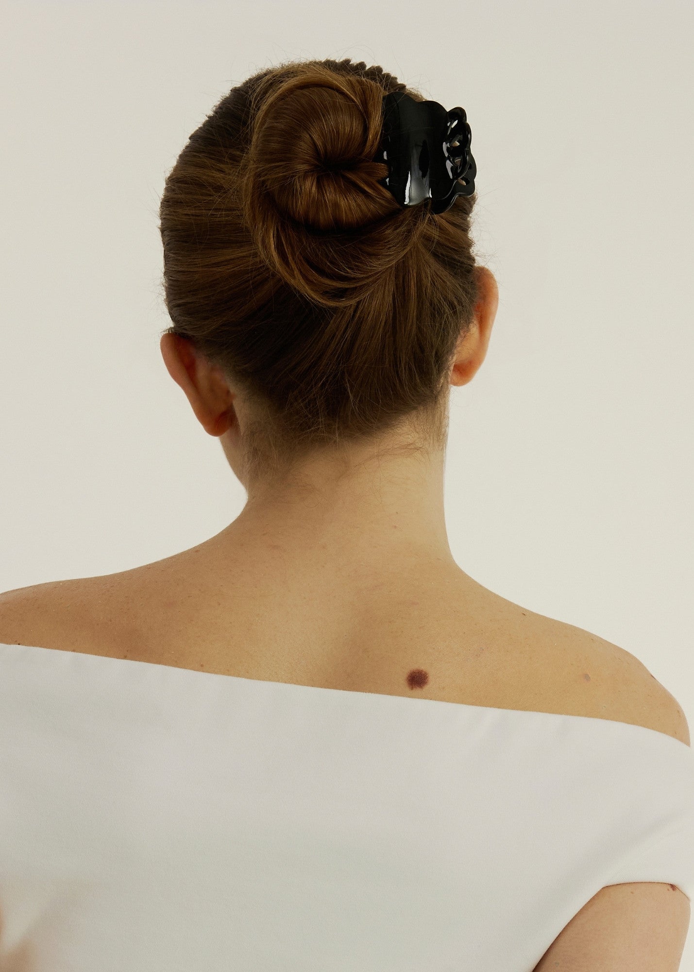 Woman with long hair tied styled half-up, half-down secured with a small black hair clip that has scalloped edges and tear drop shaped cut outs, wearing a white tank top.