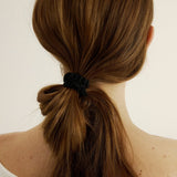Back view of a person with long brown hair tied in a ponytail with a black scrunchie on a light background