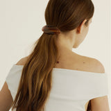 Woman with long, dark hair using the Oval Barrette in Honey against a plain background