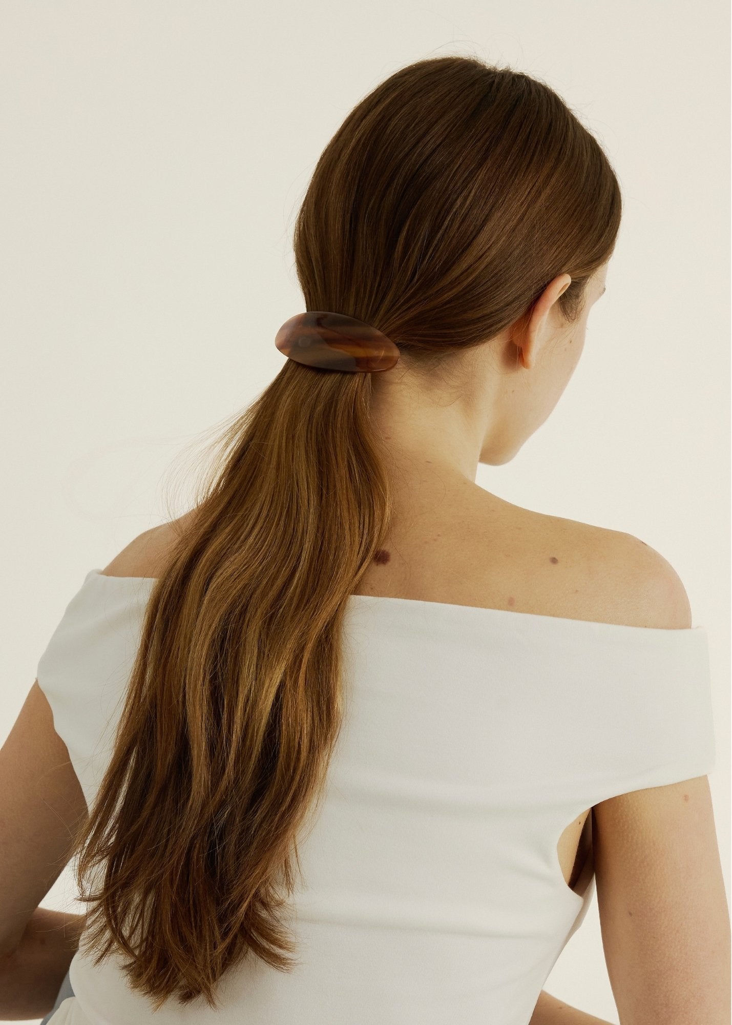 Woman with long, dark hair using the Oval Barrette in Honey against a plain background