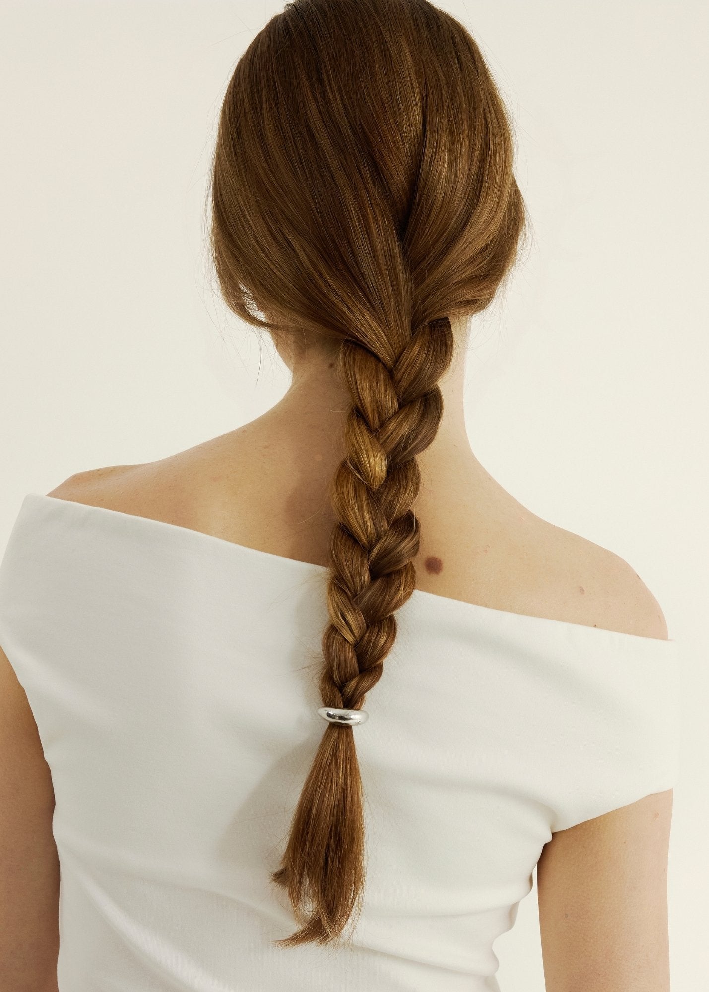 Woman with braided hair with a hair cuff
wearing a white off-shoulder top on a plain background