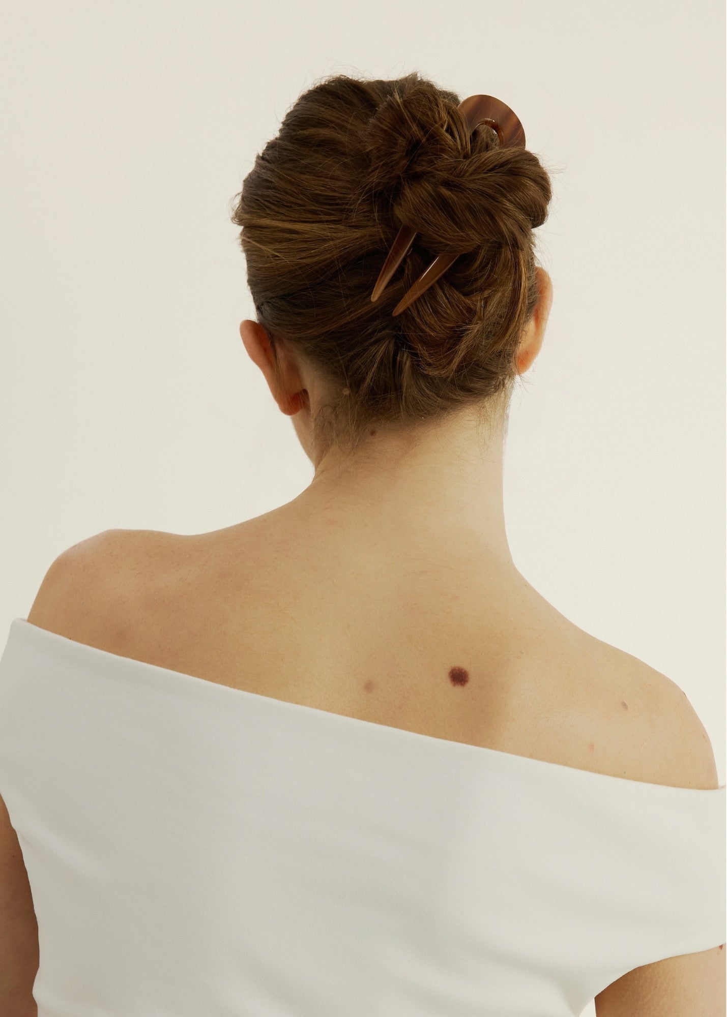 Person with a bun secured with the French Pin in Honey wearing a white tank top against a plain background