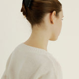 Woman with dark brown hair styled in a bun secured with the Demi Clip in Black, wearing a white sweater against a white background
