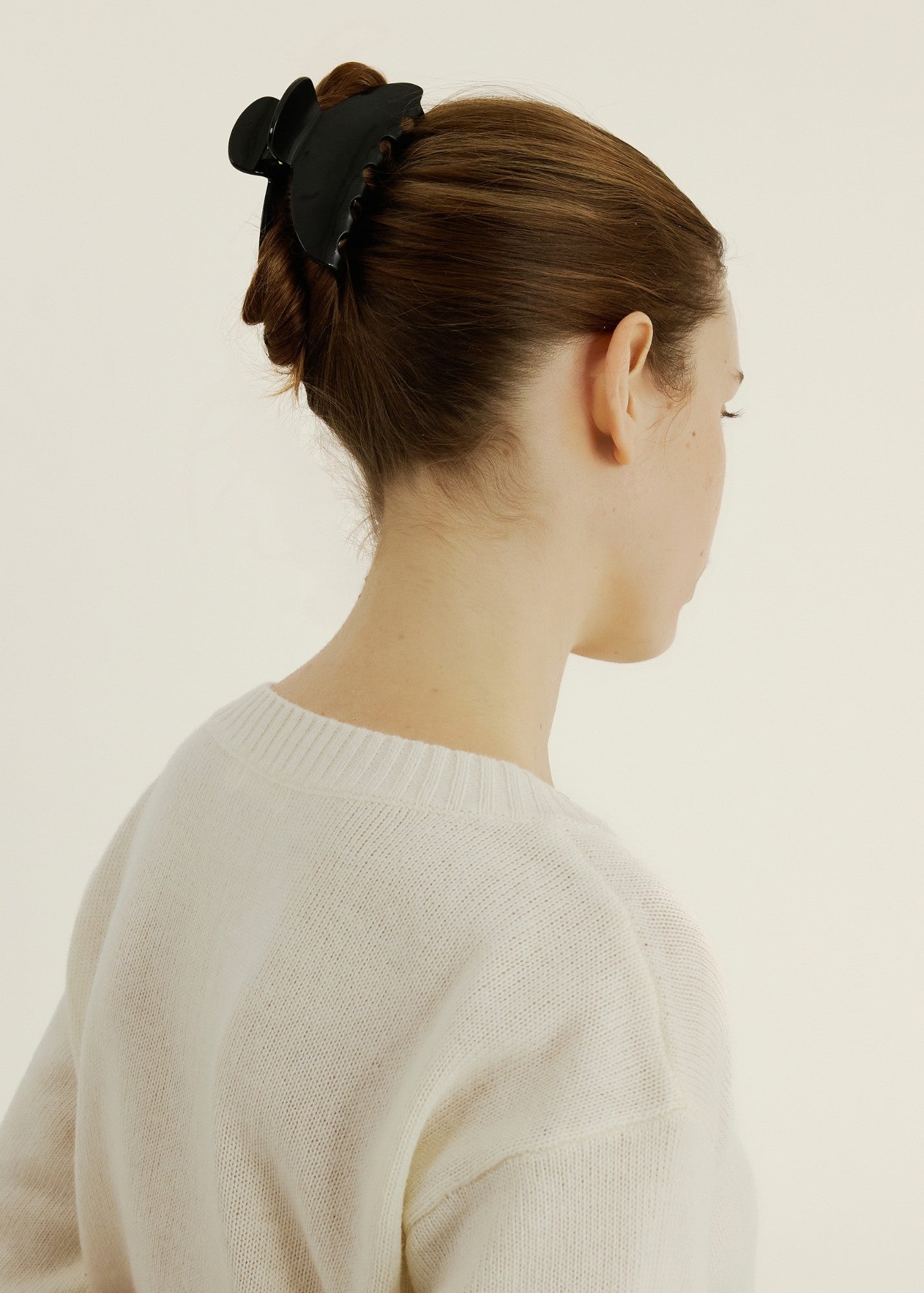Woman with dark brown hair styled in a bun secured with the Demi Clip in Black, wearing a white sweater against a white background