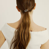 Woman with long brown hair tied in a ponytail hair cuff wearing a white top on a light background