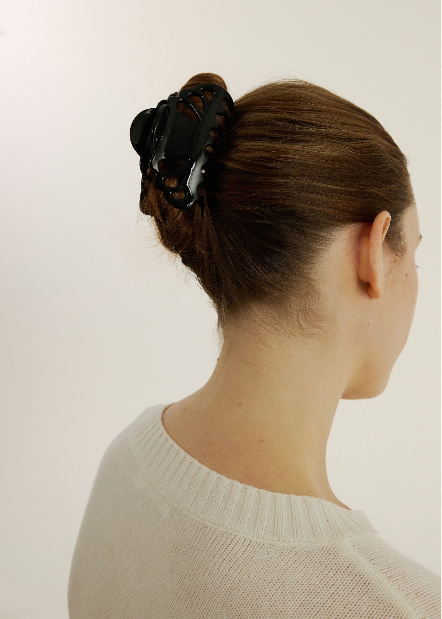Woman with hair in an up-do hairstyle secured with a medium black hair claw clip with scalloped edges and tear drop shaped cut outs wearing a white top