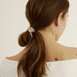 Woman with brown hair styled in a loose bun secured with the silk hair tie in champagne