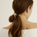 Woman with brown hair styled in a loose bun secured with the silk hair tie in champagne