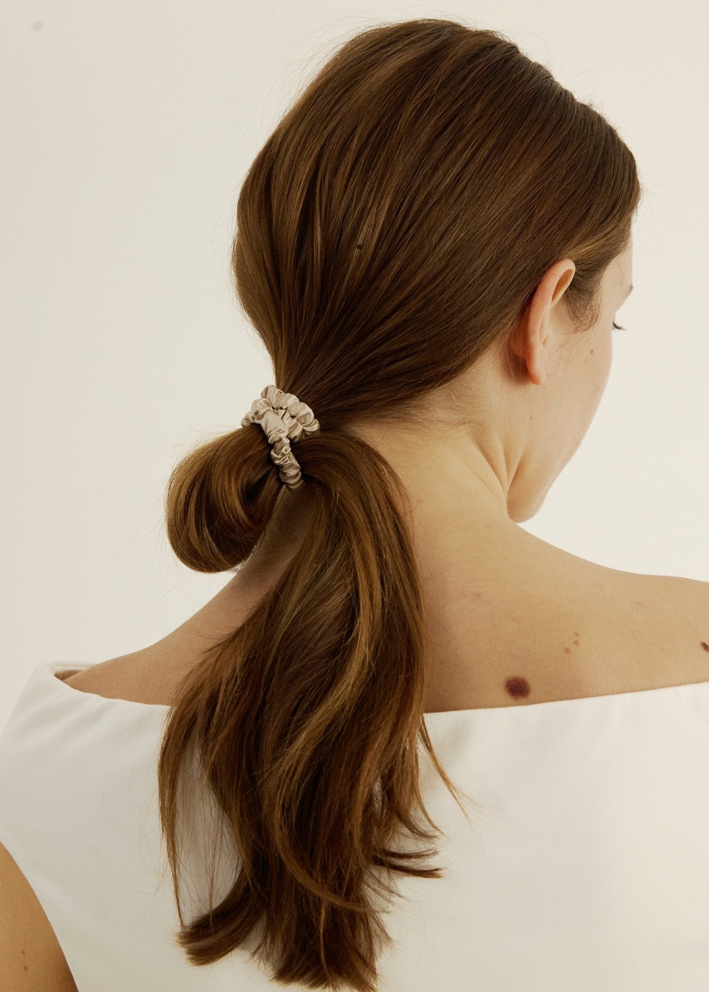 Woman with brown hair styled in a loose bun secured with the silk hair tie in champagne