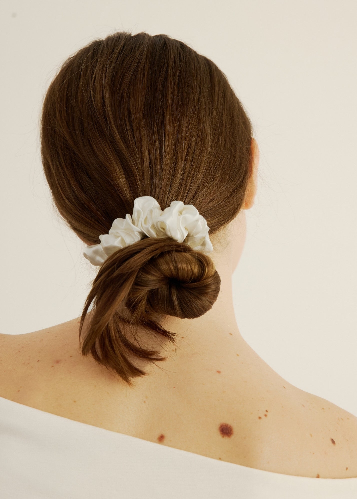 Person with a braided bun holding a white scrunchie on a plain background