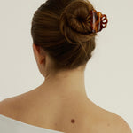 Woman wearing a white tank top with their hair in a bun secured with a small tortoise coloured hair clip that has scalloped edges.