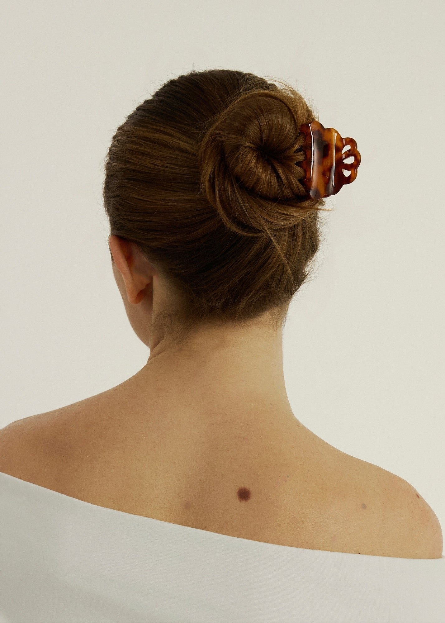 Woman wearing a white tank top with their hair in a bun secured with a small tortoise coloured hair clip that has scalloped edges.