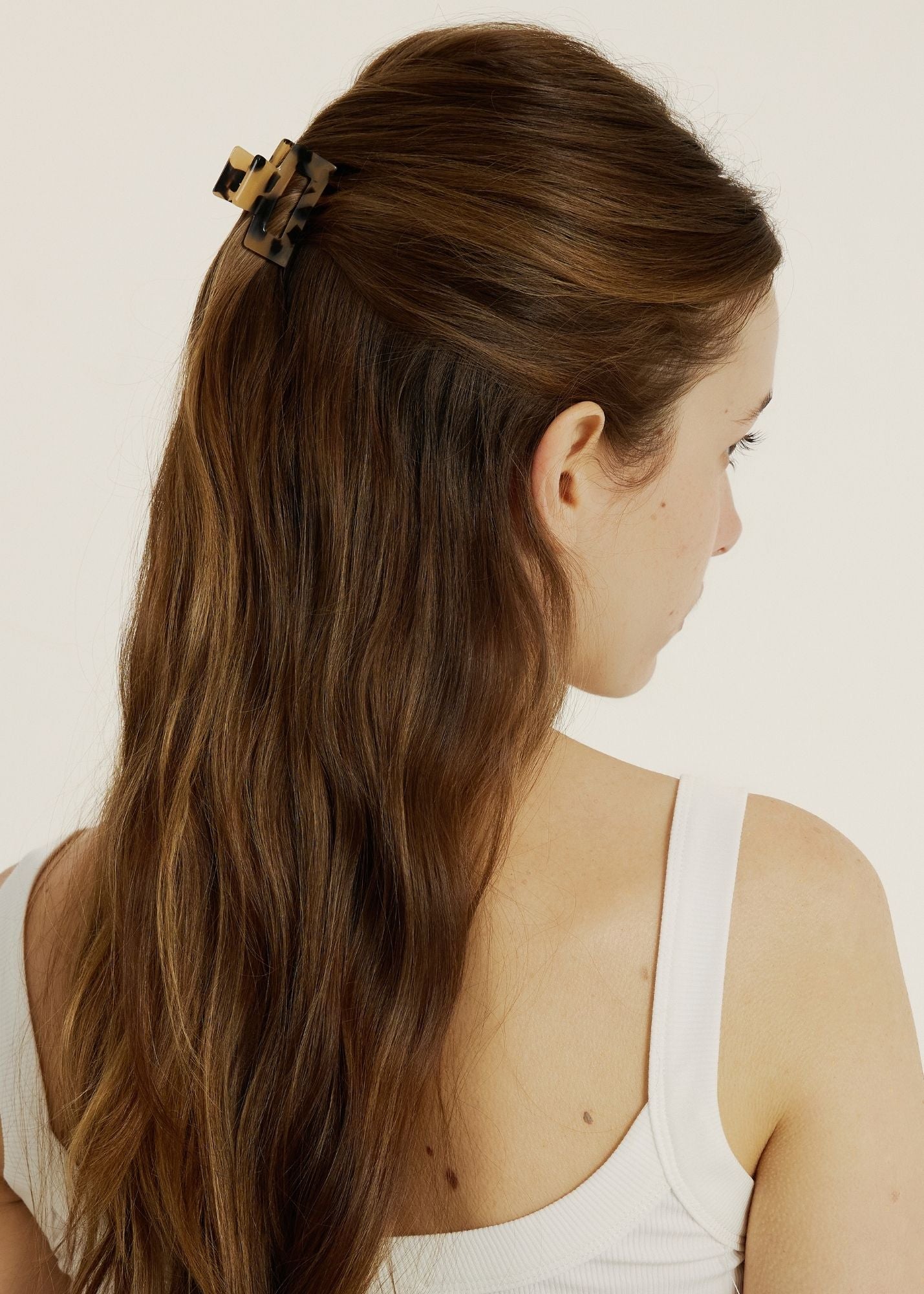 Close up of woman with dark brown hair in a half up, half down hairstyle secured with a mini light tortoise coloured hair claw clip.