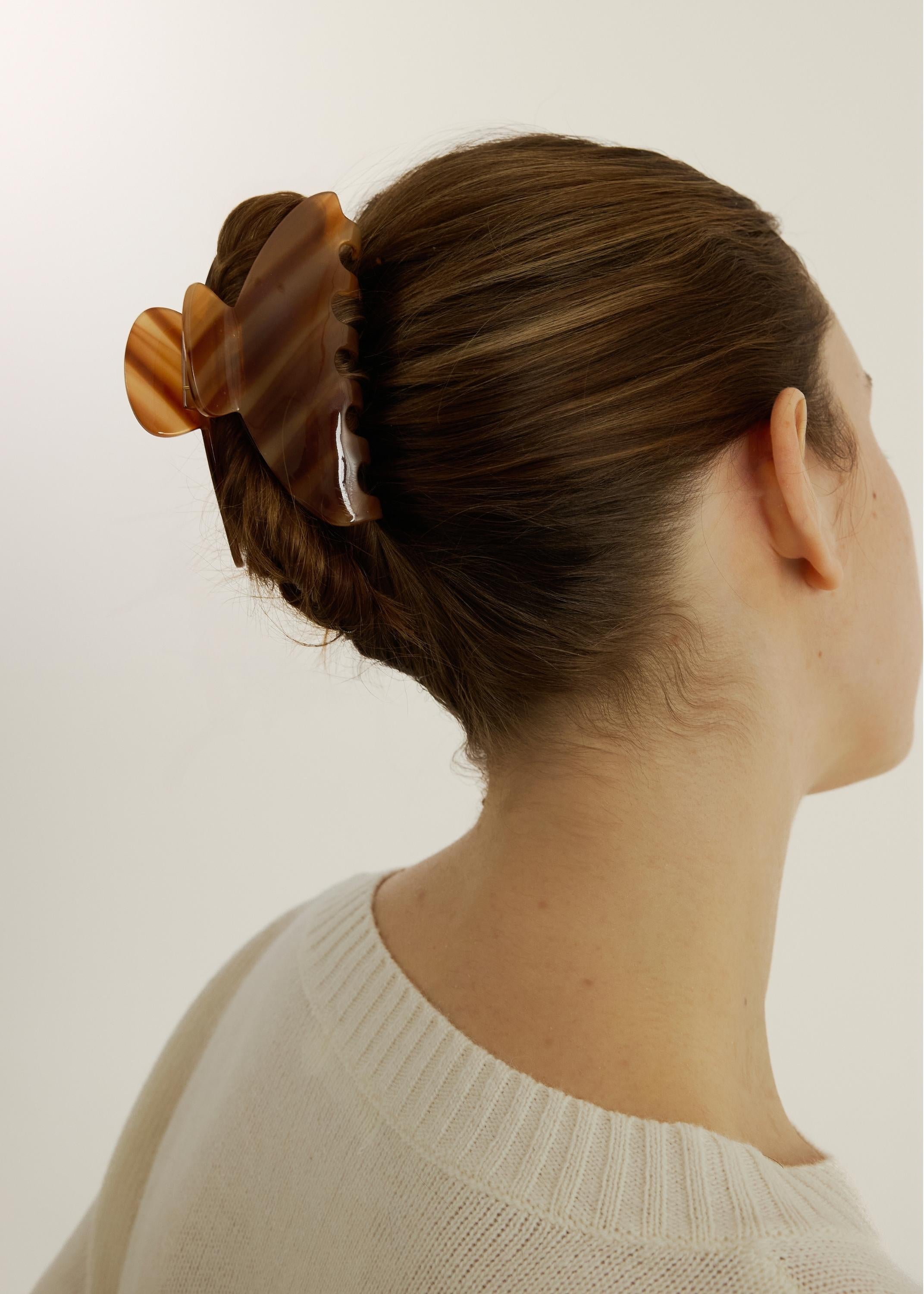 Woman with an up-do hairstyle secured with the large Demi Clip in Honey wearing a white top on a white background