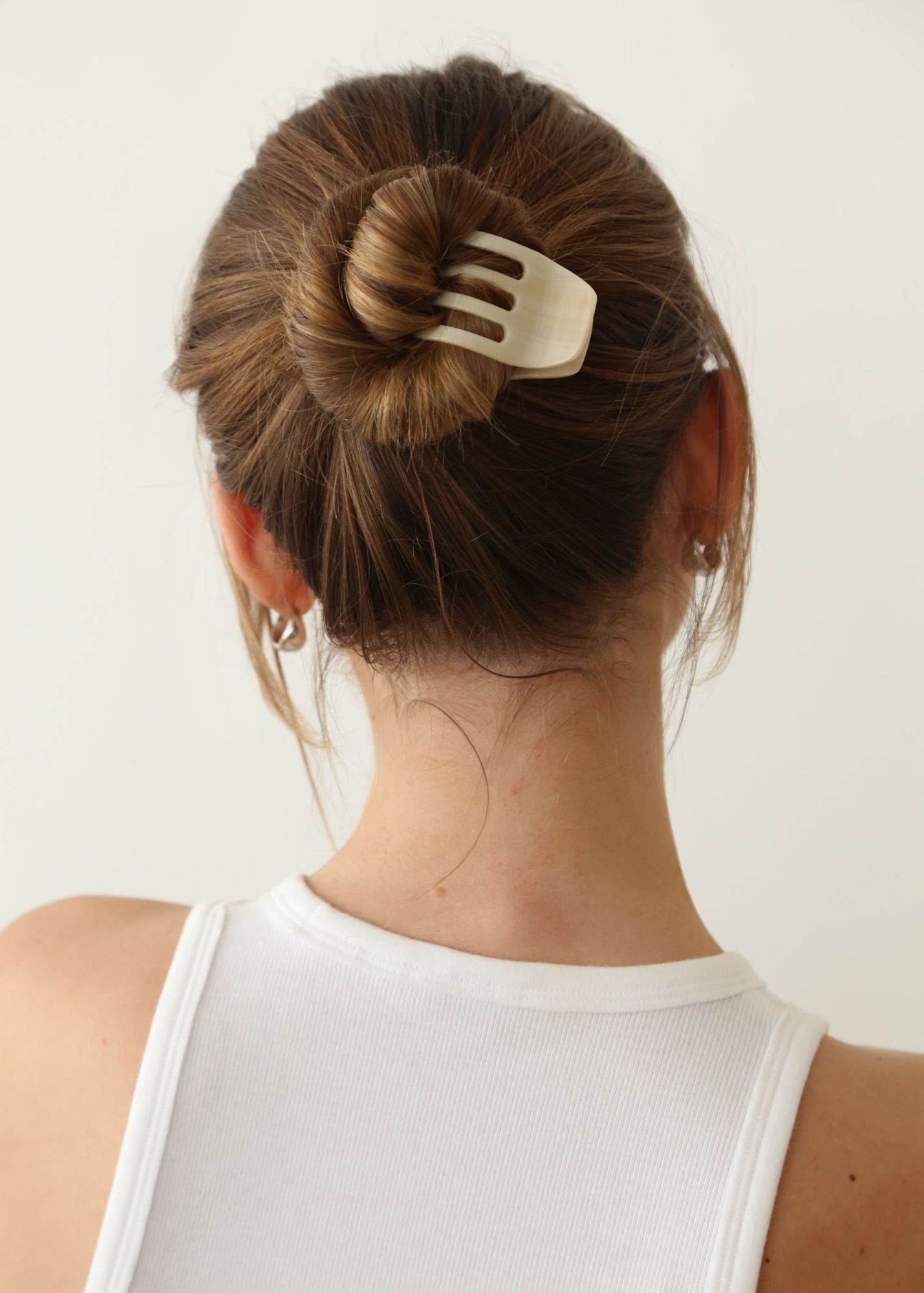 Person with a bun held in place by the Sculpt Clip in Vanilla against a plain background