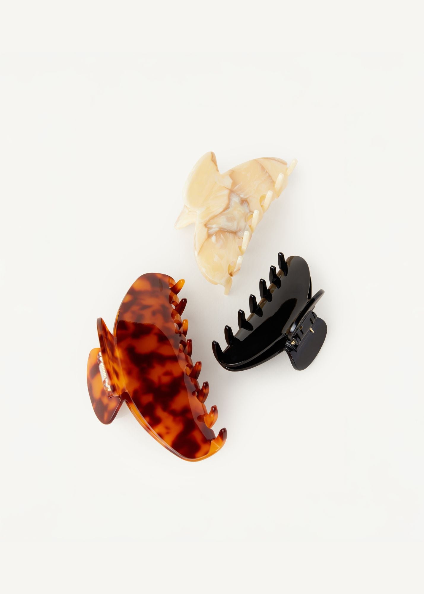 Three Demi hair clips in the colours tortoise, beige, and black on a white background